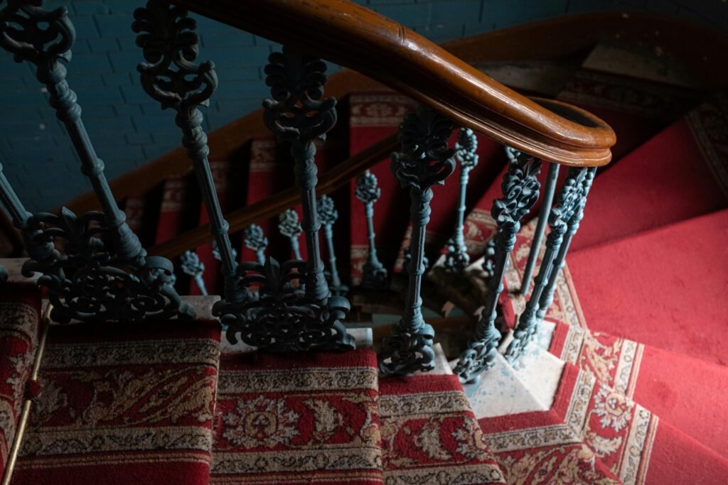Close-up of ornate vintage staircase with red carpet and wrought iron railing.