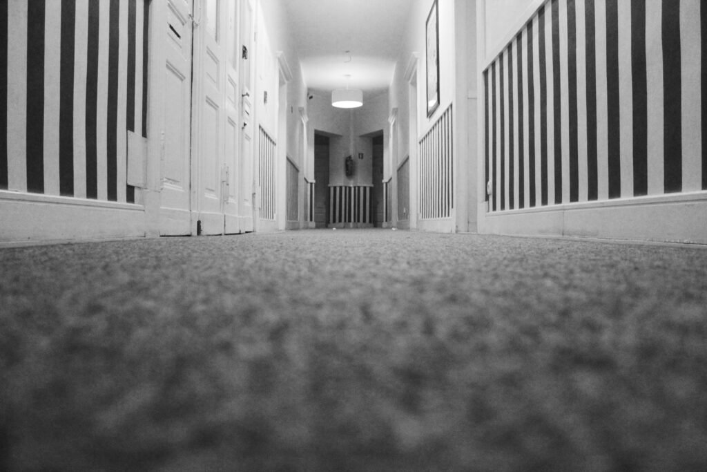 Low angle view of an empty hotel corridor with striped walls and carpet in monochrome.