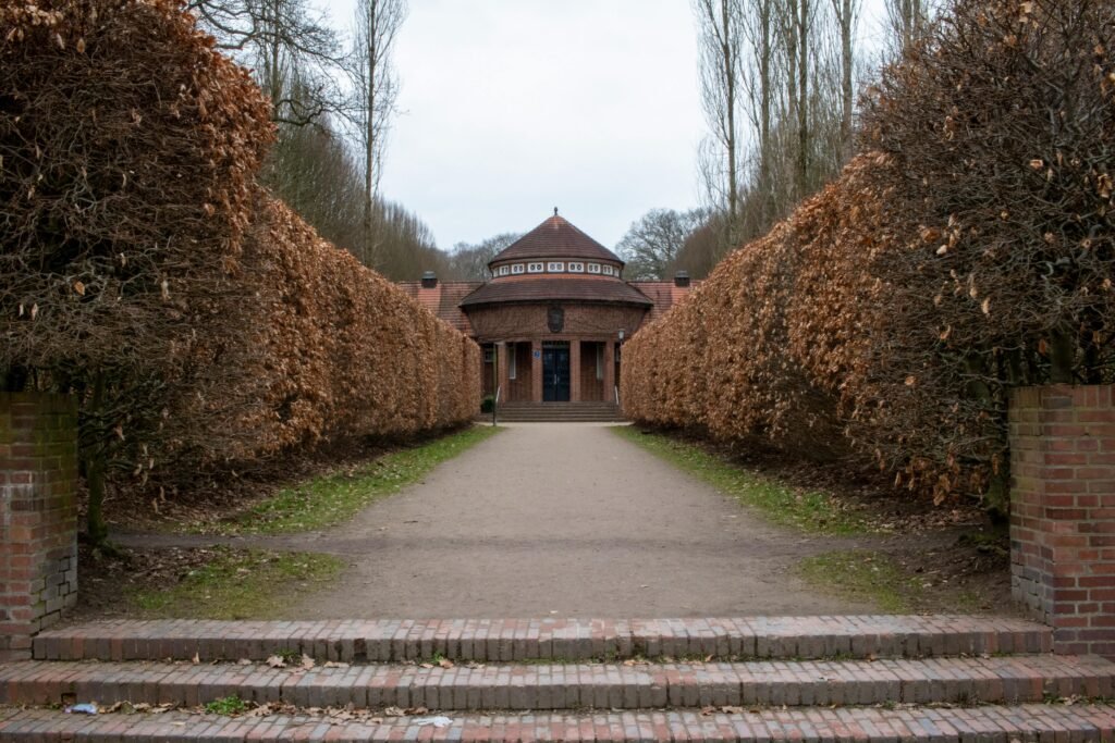A serene view of the path leading to Trinkhalle in Hamburg Park, lined with hedges and bare trees.