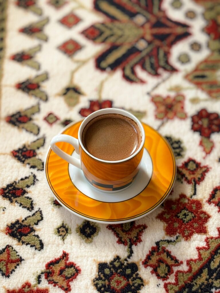 Close-up of a coffee cup with frothy top on a colorful patterned rug, creating a warm and inviting scene.
