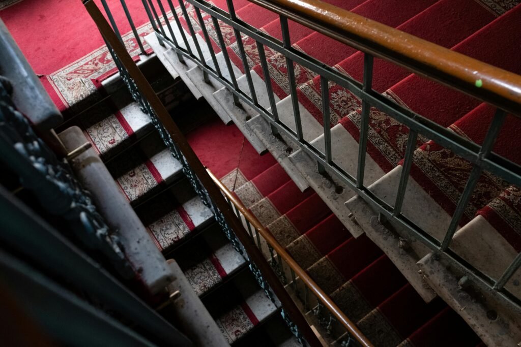 A vintage staircase with a red carpet and intricate handrail details, offering a retro perspective.