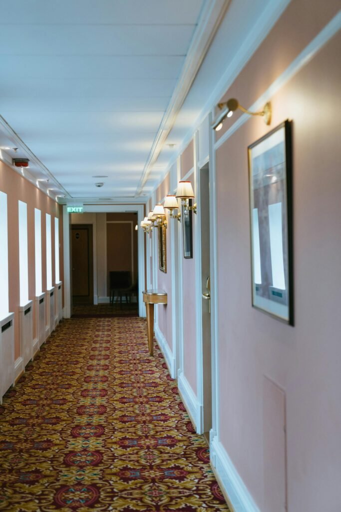 Well-lit hotel corridor with ornate carpet and framed art, offering a cozy atmosphere.